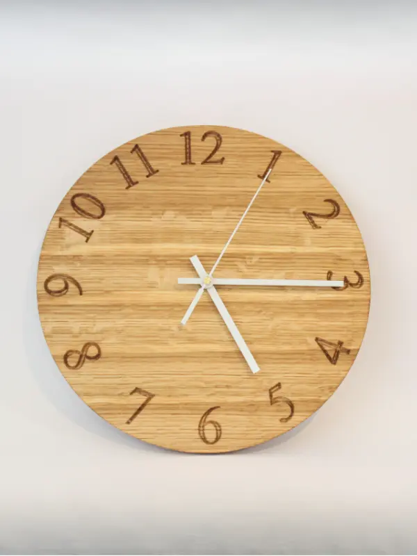 Handmade oak clock with engraved numbers 1 to 12, shown with black hands. A personalised wooden wall clock with optional engraving for names, dates, or logos.
